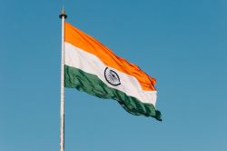 The national flag of India, hoisted at the top of a flagpole, being blown by a strong breeze.