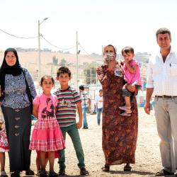A displaced family in a refugee camp, consisting of a man, three women, and four children.
