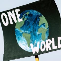 A placard at a climate protest reading 'One World', demanding social and economic justice alongside environmental justice.