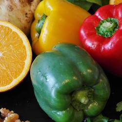 A selection of fruit and vegetables arranged on a table, including a cut-open orange, red, yellow, and green peppers, a fennel bulb and walnuts. All examples of what we can consume to achieve healthier diets.