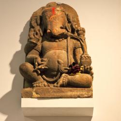 A stone statue of the Hindu goddess Ganesha, placed on a pediment high up on a wall.