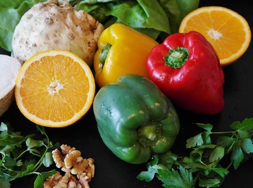 A selection of fruit and vegetables arranged on a table, including a cut-open orange, red, yellow, and green peppers, a fennel bulb and walnuts. All examples of what we can consume to achieve healthier diets.