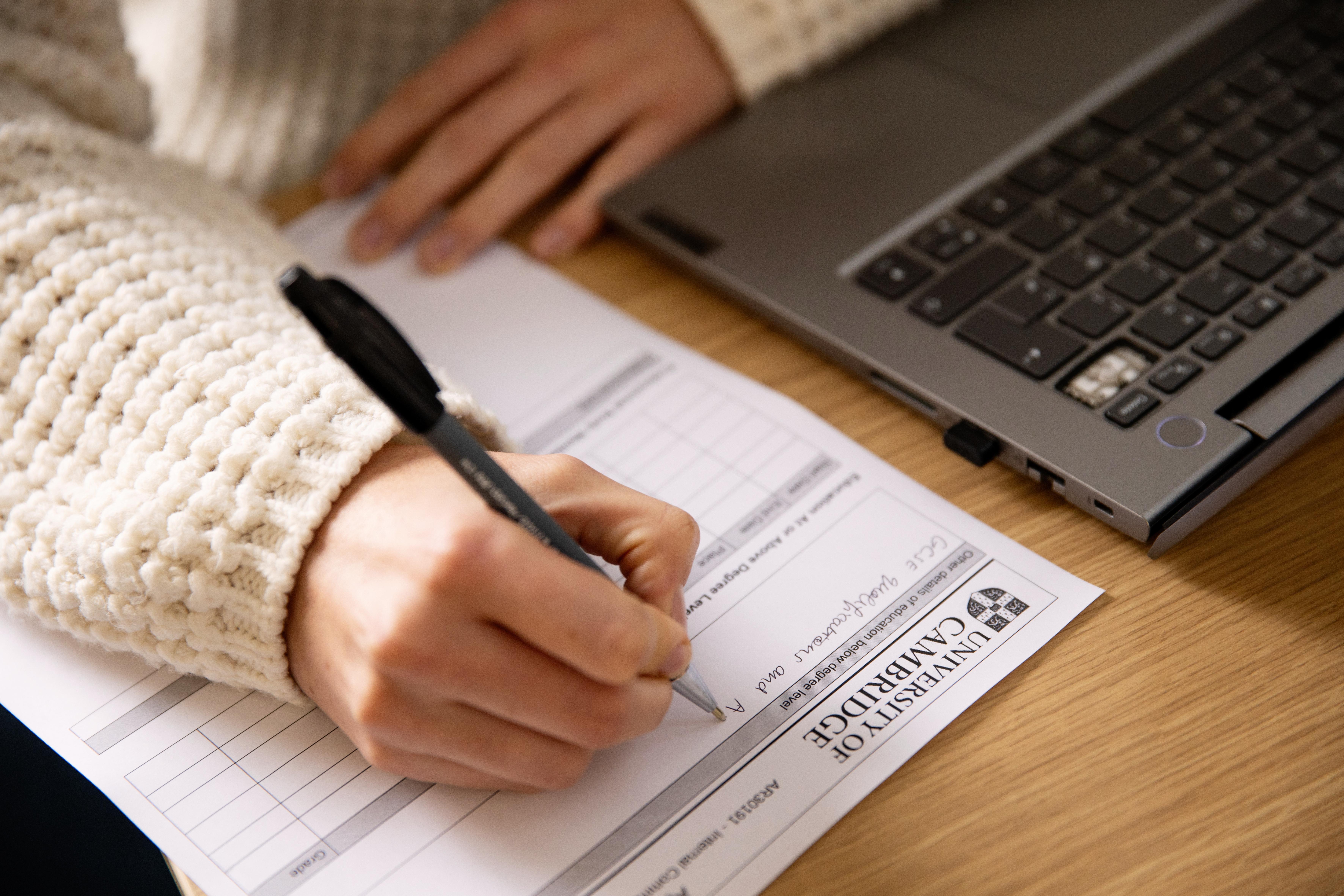 A University staff member working and writing on a paper form at the Old Cavendish Copyright: University of Cambridge (November 2024)