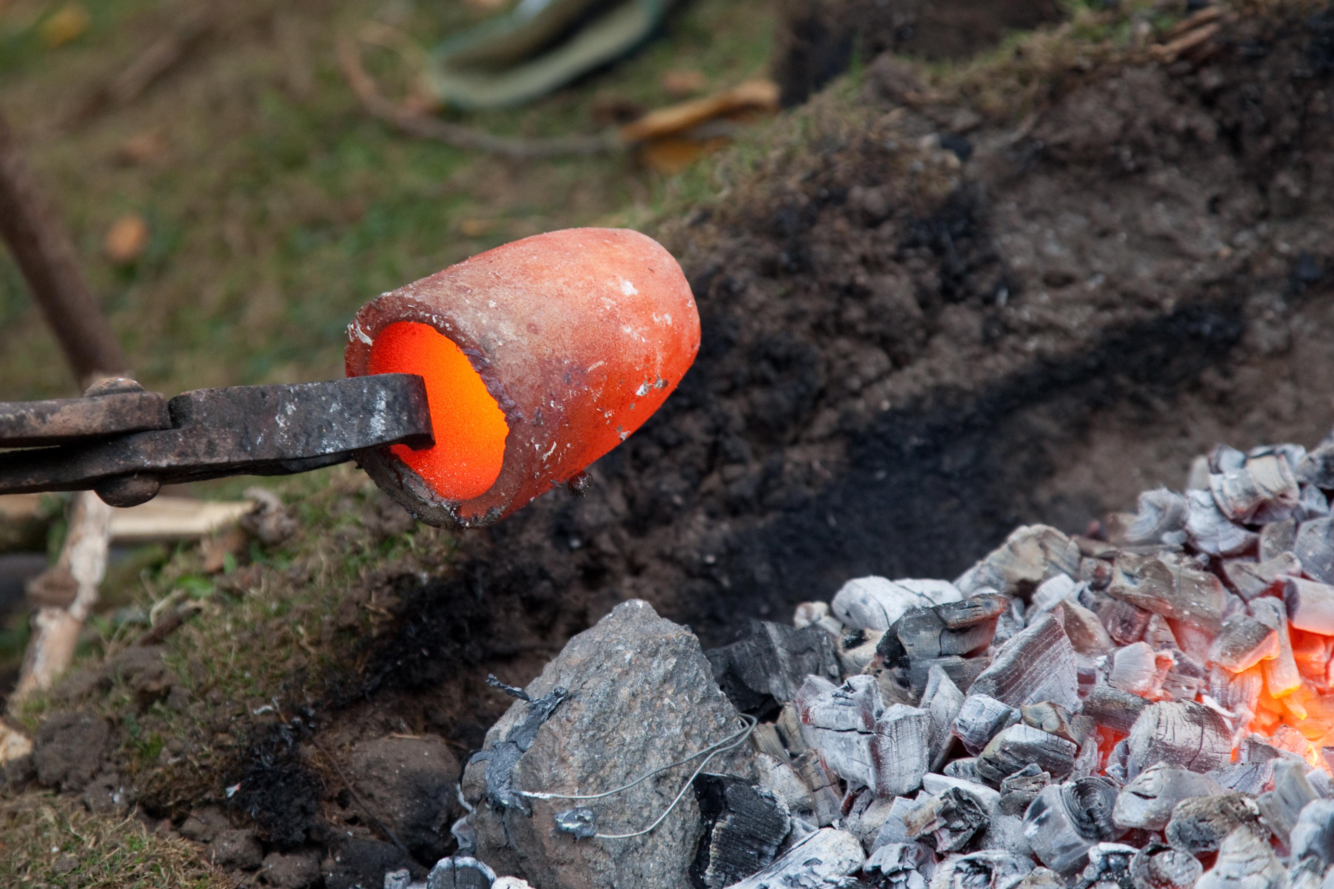 A glowing metal cup being pulled from a fire with a pair of clamps. Festival of Ideas demonstration.